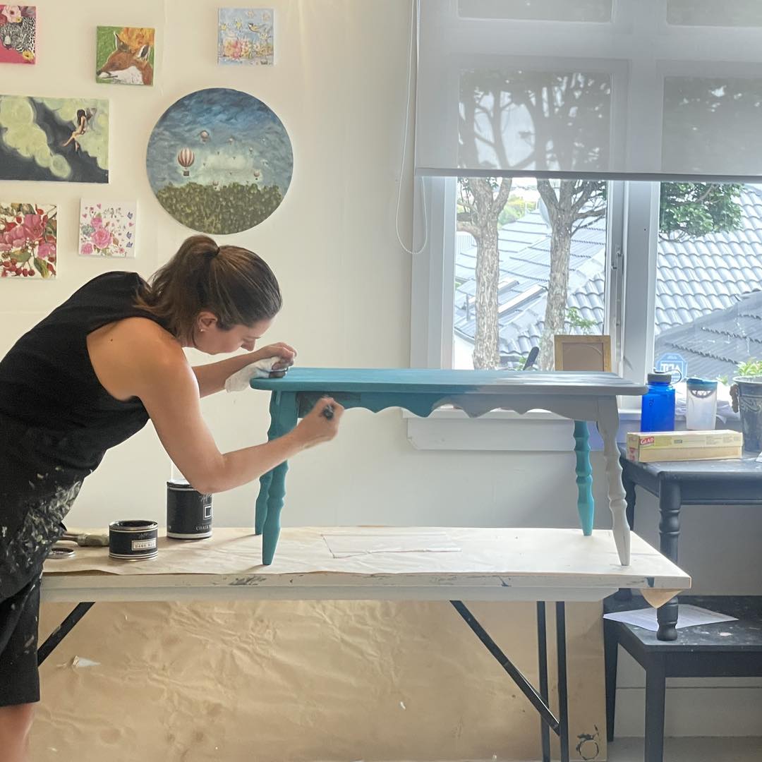 Woman demonstrating painting a wooden table 