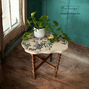 Small wooden table with floral design on a wooden floor, featuring a plant and decorative item.
